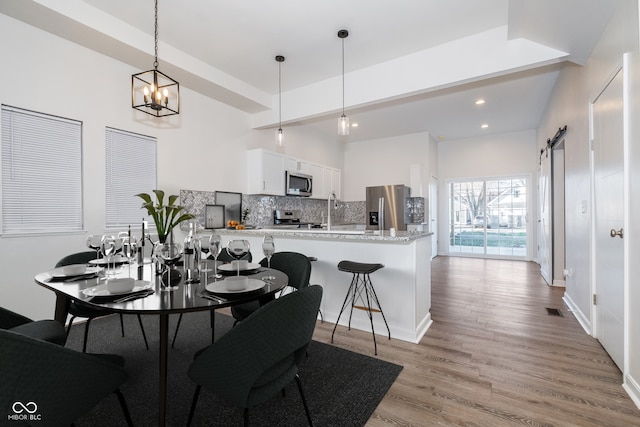 dining area with an inviting chandelier, sink, a barn door, light wood-type flooring, and beamed ceiling