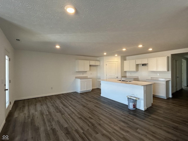 kitchen with sink, a kitchen island with sink, dark hardwood / wood-style floors, a textured ceiling, and white cabinets