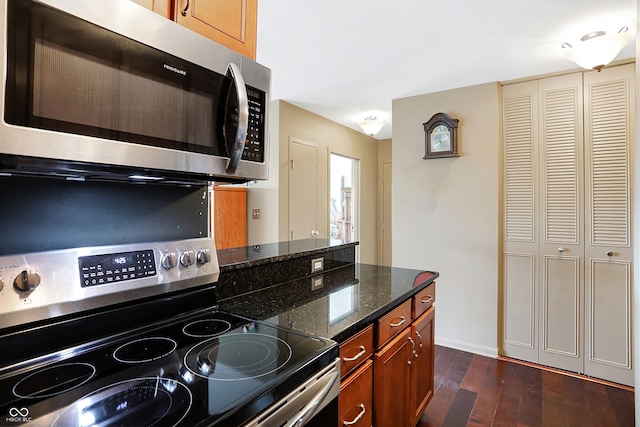 kitchen featuring dark wood-type flooring, stainless steel appliances, and dark stone counters