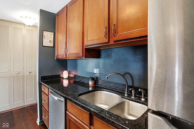 kitchen with stainless steel appliances, dark hardwood / wood-style floors, dark stone counters, and sink