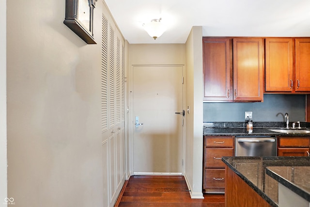 kitchen with stainless steel dishwasher, dark stone countertops, sink, and dark wood-type flooring