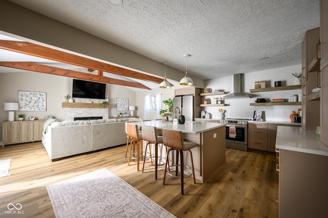 kitchen with a kitchen breakfast bar, an island with sink, wall chimney range hood, pendant lighting, and appliances with stainless steel finishes