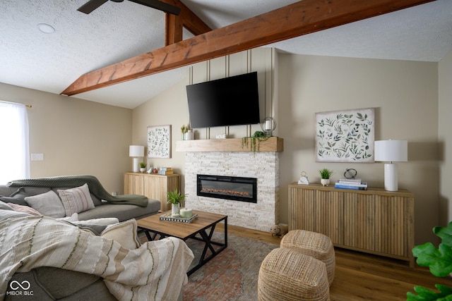 living room featuring a stone fireplace, lofted ceiling with beams, ceiling fan, dark wood-type flooring, and a textured ceiling