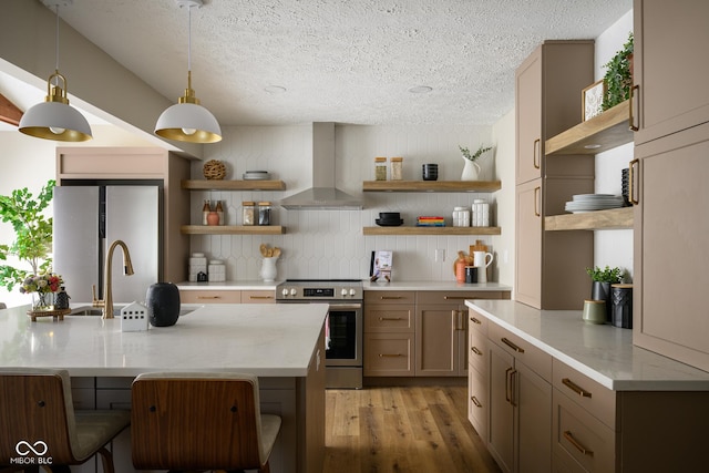 kitchen with stainless steel appliances, wall chimney exhaust hood, a kitchen breakfast bar, light wood-type flooring, and hanging light fixtures