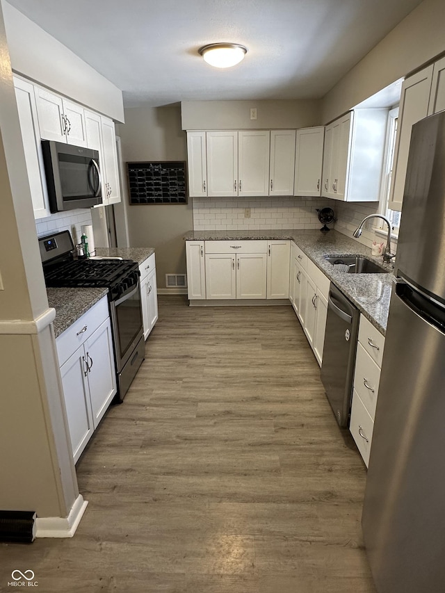 kitchen with white cabinetry, sink, light hardwood / wood-style flooring, backsplash, and appliances with stainless steel finishes