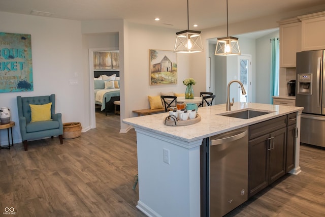 kitchen featuring light stone countertops, sink, decorative light fixtures, a center island with sink, and appliances with stainless steel finishes