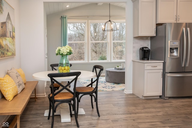 dining space with dark wood-type flooring, an inviting chandelier, vaulted ceiling, and a healthy amount of sunlight