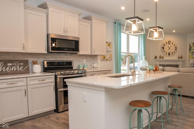 kitchen with sink, an island with sink, hanging light fixtures, and appliances with stainless steel finishes