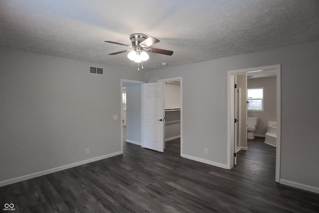 unfurnished bedroom featuring a walk in closet, dark wood-type flooring, a textured ceiling, and a closet