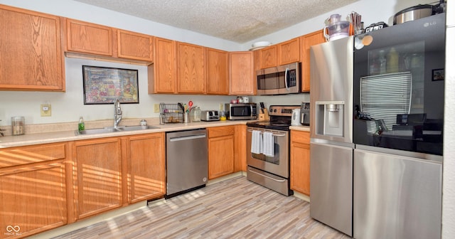 kitchen featuring light wood-type flooring, appliances with stainless steel finishes, sink, and a textured ceiling