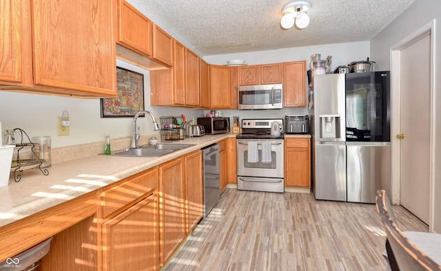 kitchen featuring sink, a textured ceiling, appliances with stainless steel finishes, and light wood-type flooring