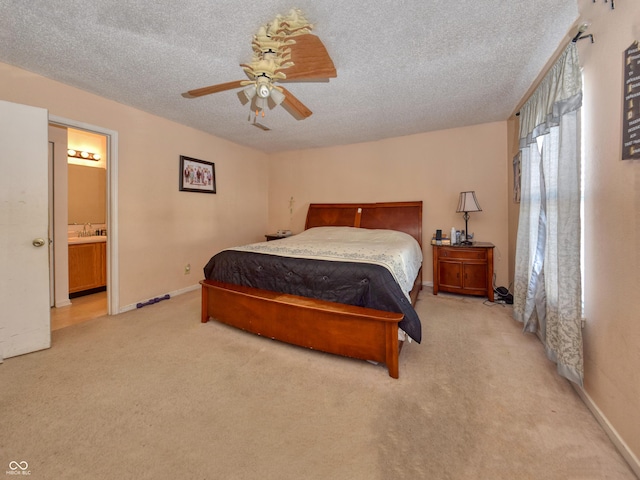 bedroom with ceiling fan, light colored carpet, a textured ceiling, and ensuite bath