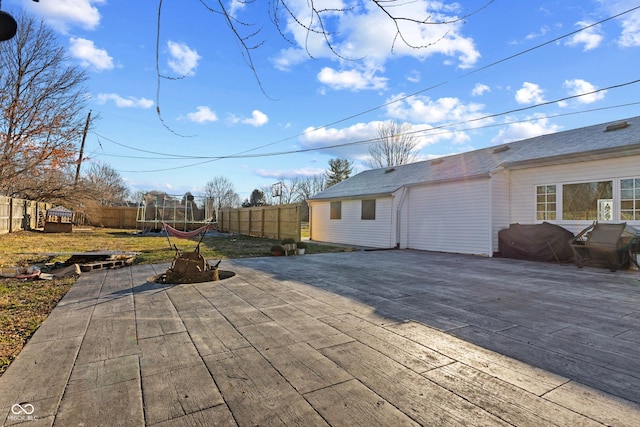 wooden terrace with driveway, a patio area, a trampoline, and a fenced backyard