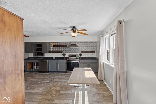 kitchen featuring open shelves, a ceiling fan, wall chimney exhaust hood, appliances with stainless steel finishes, and dark countertops