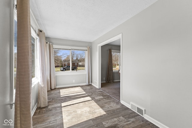 interior space with wood finished floors, a textured ceiling, baseboards, and visible vents