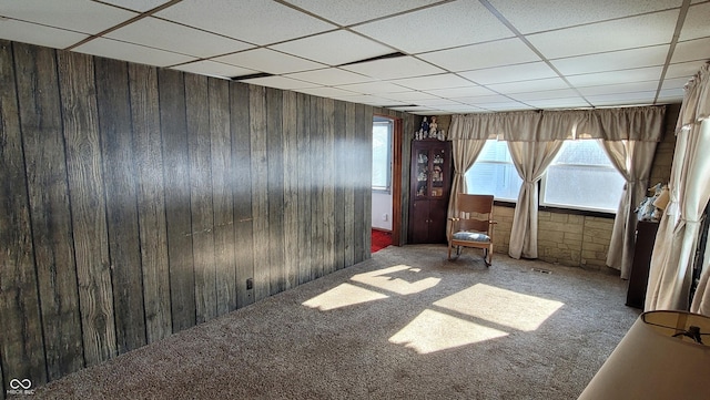 empty room with a paneled ceiling, wood walls, and dark colored carpet