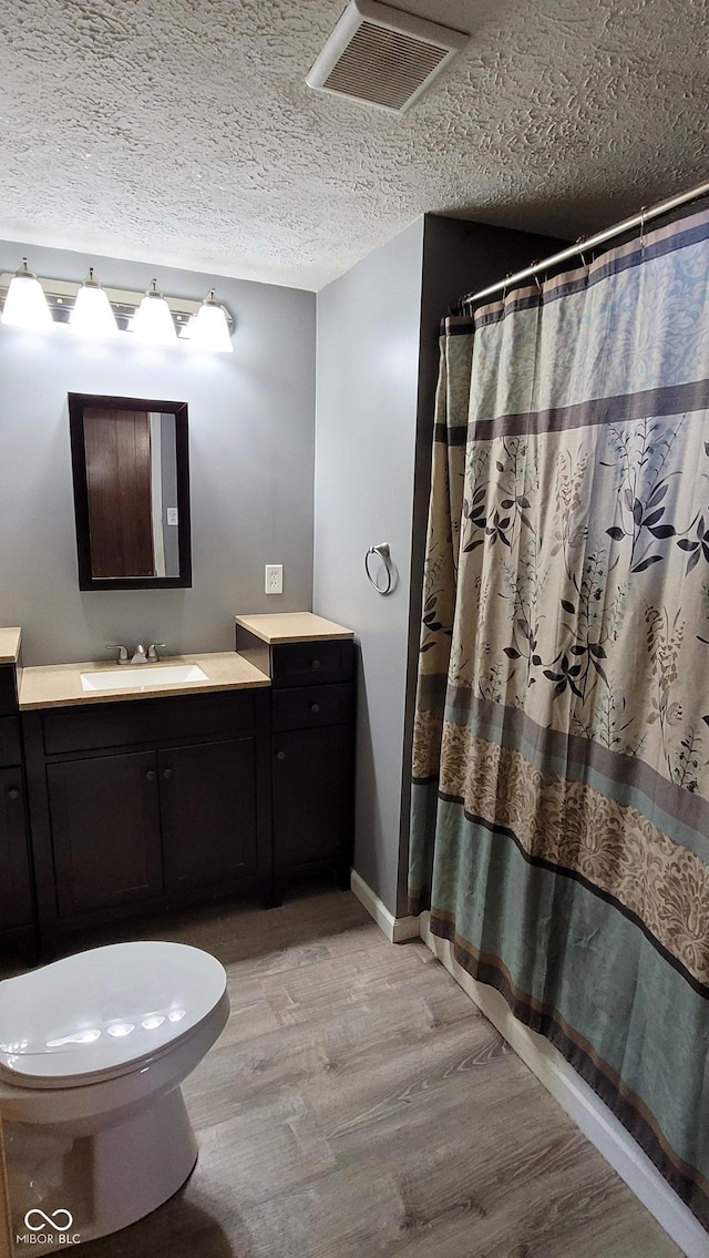 bathroom with hardwood / wood-style floors, toilet, walk in shower, vanity, and a textured ceiling