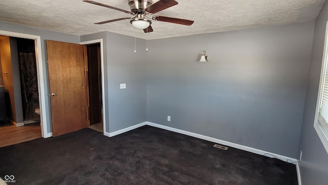 unfurnished room with a textured ceiling, ceiling fan, and dark colored carpet