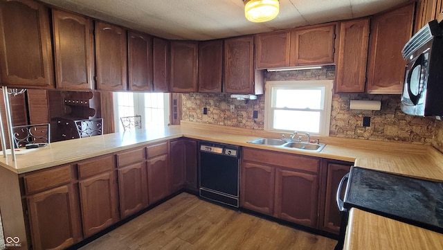 kitchen with kitchen peninsula, black appliances, tasteful backsplash, light wood-type flooring, and sink