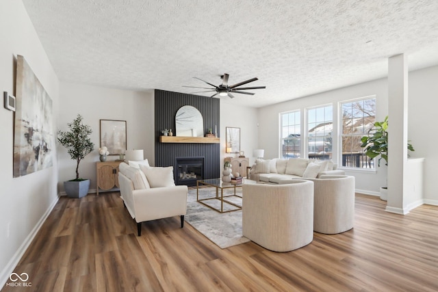 living room featuring a fireplace, wood-type flooring, a textured ceiling, and ceiling fan