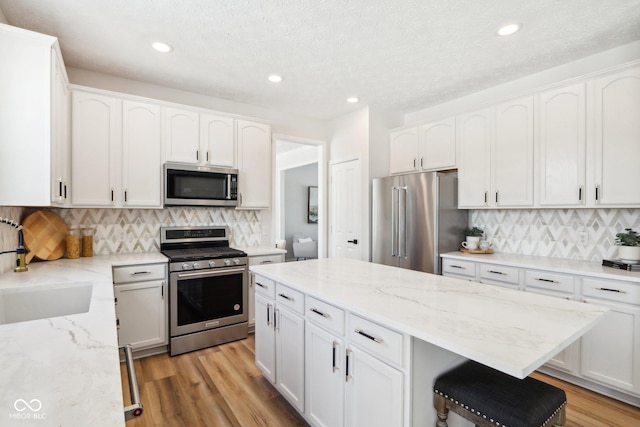 kitchen with white cabinets, appliances with stainless steel finishes, backsplash, and light stone counters