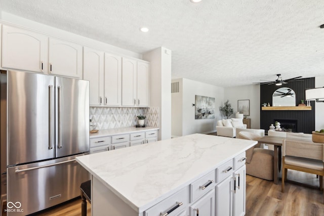 kitchen featuring white cabinetry, a large fireplace, high end refrigerator, and tasteful backsplash