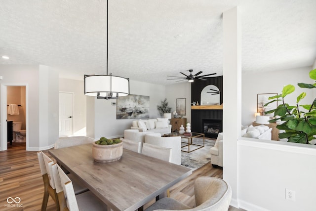 dining area featuring ceiling fan, a large fireplace, wood-type flooring, and a textured ceiling