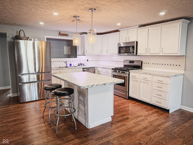 kitchen with dark wood-style floors, a center island, light countertops, appliances with stainless steel finishes, and a sink