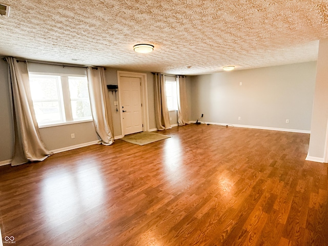 empty room with visible vents, a textured ceiling, baseboards, and wood finished floors