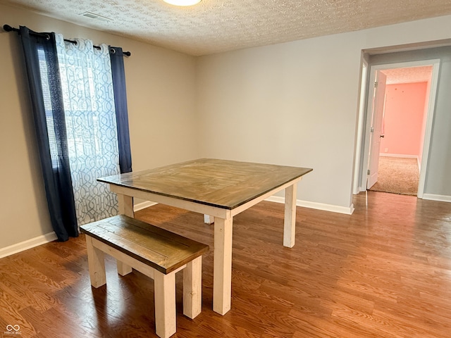 unfurnished dining area with a textured ceiling, baseboards, and wood finished floors