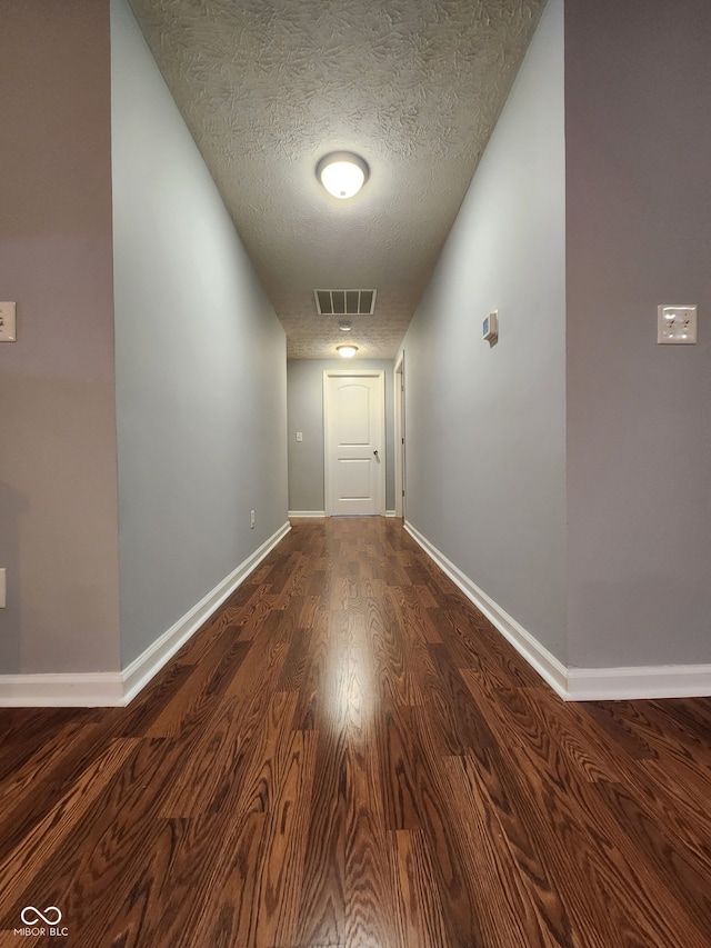 corridor with dark wood-style flooring, visible vents, a textured ceiling, and baseboards