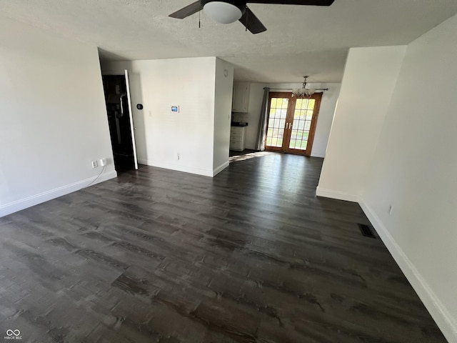 spare room with a textured ceiling, ceiling fan with notable chandelier, dark wood-type flooring, and french doors