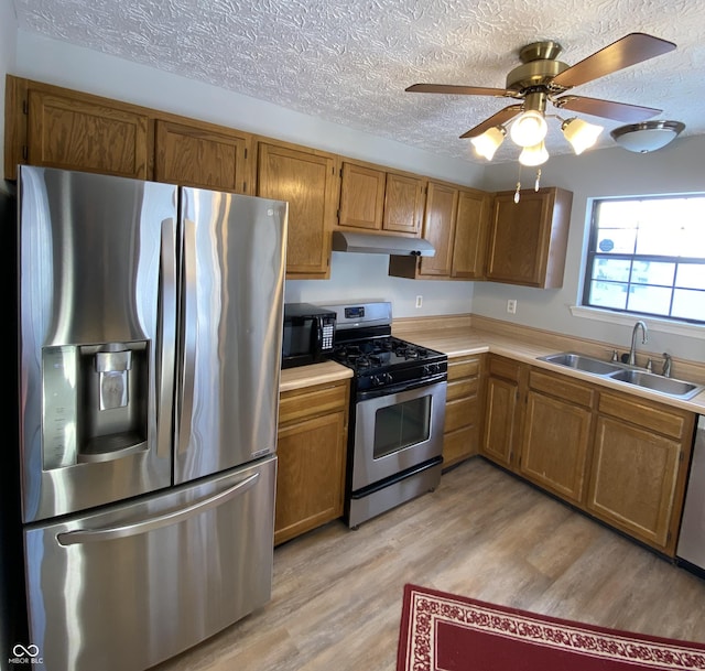 kitchen with sink, light wood-type flooring, a textured ceiling, and appliances with stainless steel finishes