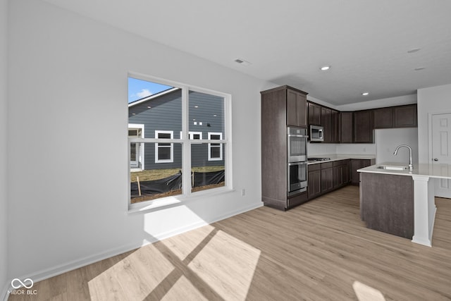 kitchen featuring stainless steel microwave, dark brown cabinets, visible vents, light wood-style floors, and a sink