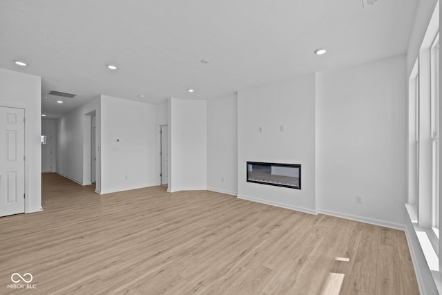 unfurnished living room featuring a glass covered fireplace, recessed lighting, and light wood-style floors