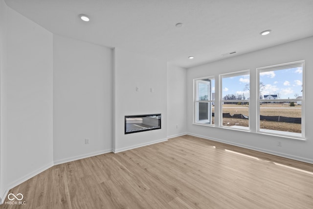 unfurnished living room featuring visible vents, baseboards, recessed lighting, light wood-style floors, and a glass covered fireplace