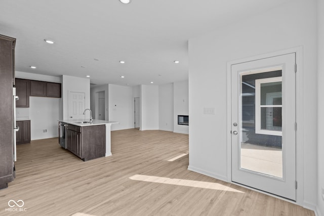 kitchen with dark brown cabinets, open floor plan, light wood finished floors, and a sink