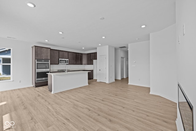 kitchen with dark brown cabinets, recessed lighting, light wood-style flooring, stainless steel appliances, and a kitchen island with sink