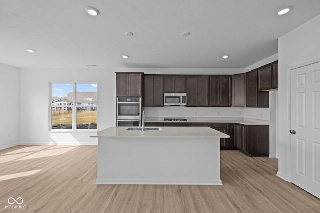 kitchen featuring an island with sink, light wood-style flooring, a sink, stainless steel appliances, and light countertops