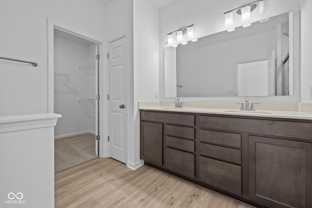 full bathroom featuring double vanity, a spacious closet, wood finished floors, and a sink