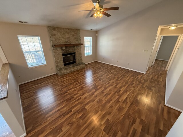 unfurnished living room with a healthy amount of sunlight, dark hardwood / wood-style flooring, a stone fireplace, and lofted ceiling