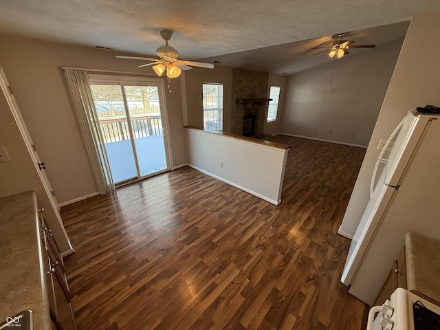 unfurnished living room with a textured ceiling, ceiling fan, dark hardwood / wood-style flooring, and a fireplace