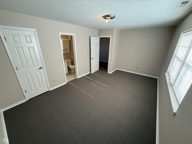 unfurnished bedroom with dark colored carpet, a textured ceiling, and connected bathroom