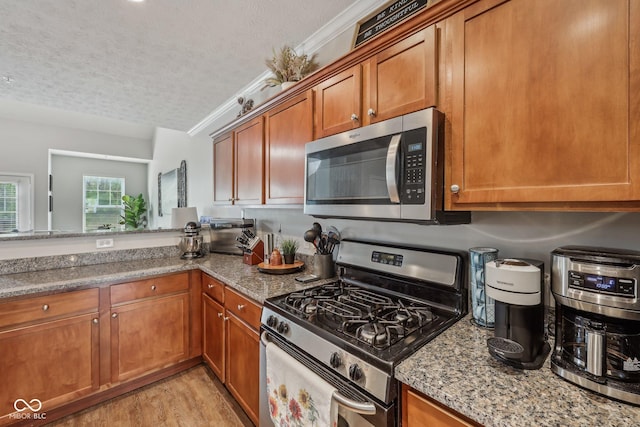 6595 Reserve Dr, Indianapolis, IN 46220 - kitchen featuring stainless steel appliances, a textured ceiling, brown cabinetry, light stone counters, and light wood-style floors