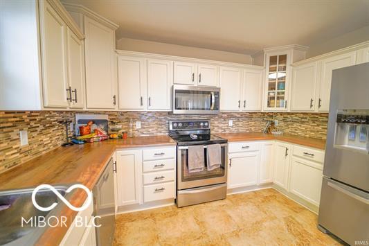 kitchen with butcher block counters, white cabinetry, decorative backsplash, and appliances with stainless steel finishes