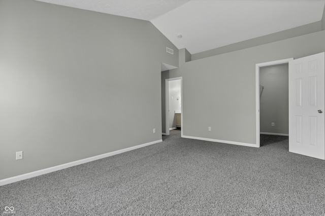 unfurnished bedroom with a walk in closet, ensuite bath, dark carpet, and vaulted ceiling