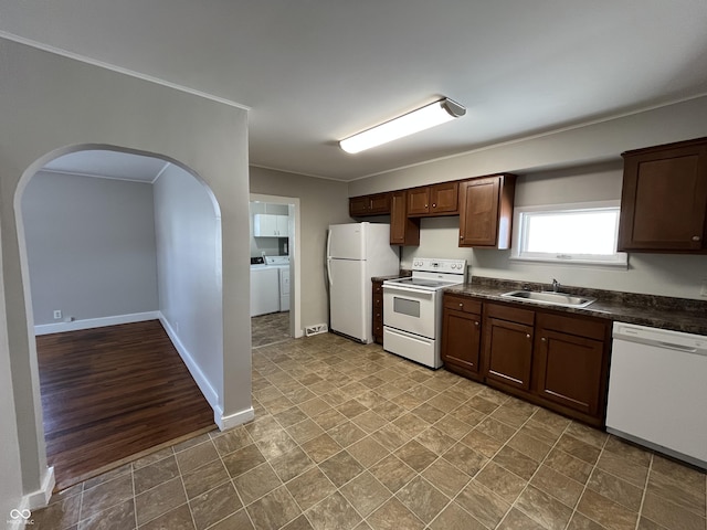 kitchen with a sink, dark countertops, white appliances, arched walkways, and washing machine and clothes dryer