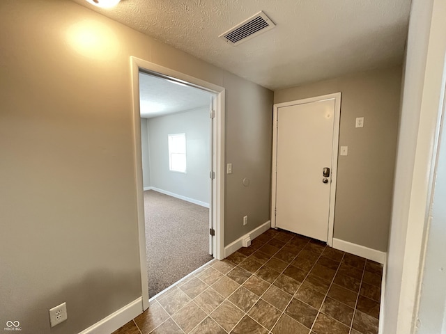 foyer entrance featuring visible vents, a textured ceiling, baseboards, and dark colored carpet