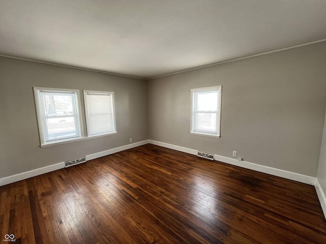 empty room with dark wood-style floors, visible vents, and baseboards