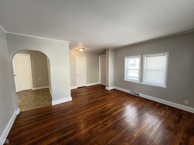 unfurnished room with visible vents, crown molding, dark wood-type flooring, baseboards, and arched walkways